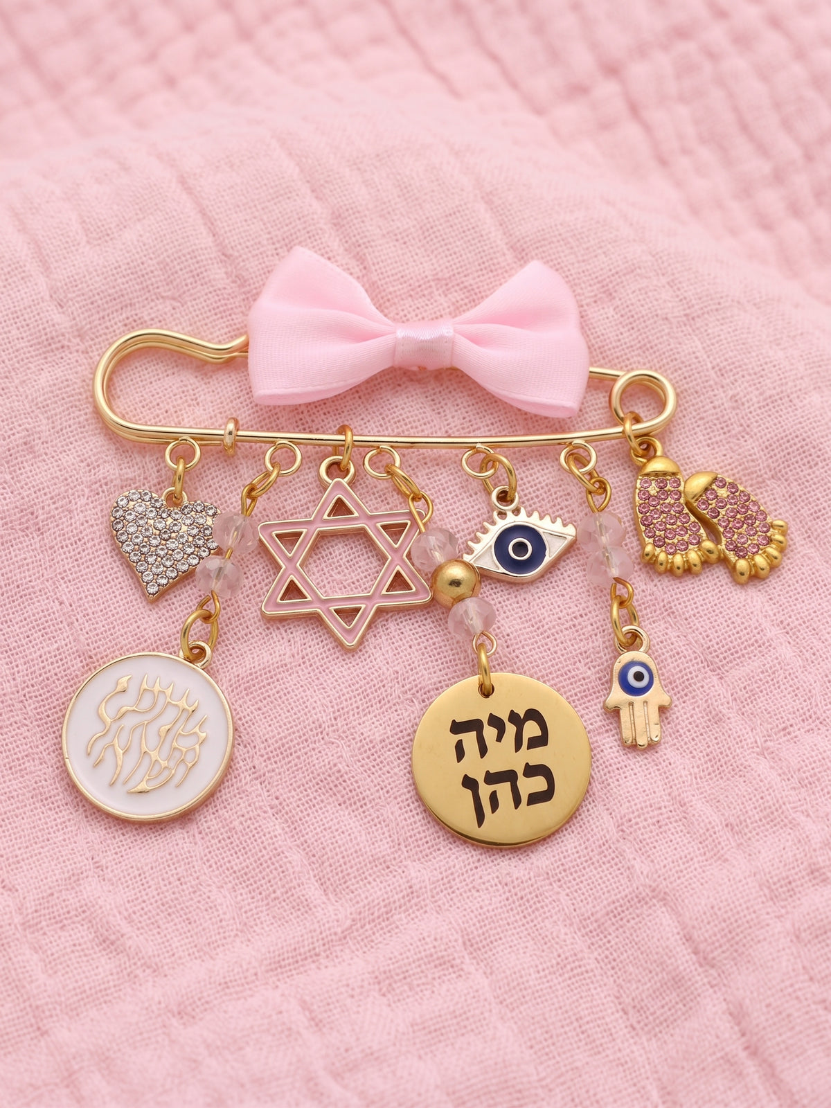 סיכת עגלה יוקרתית לתינוקת בצבע זהב ורוד עם תליוני מזל, חמסה ועין הרע, כולל חריטה אישית של שם התינוקת על רקע חיתול טטרה.